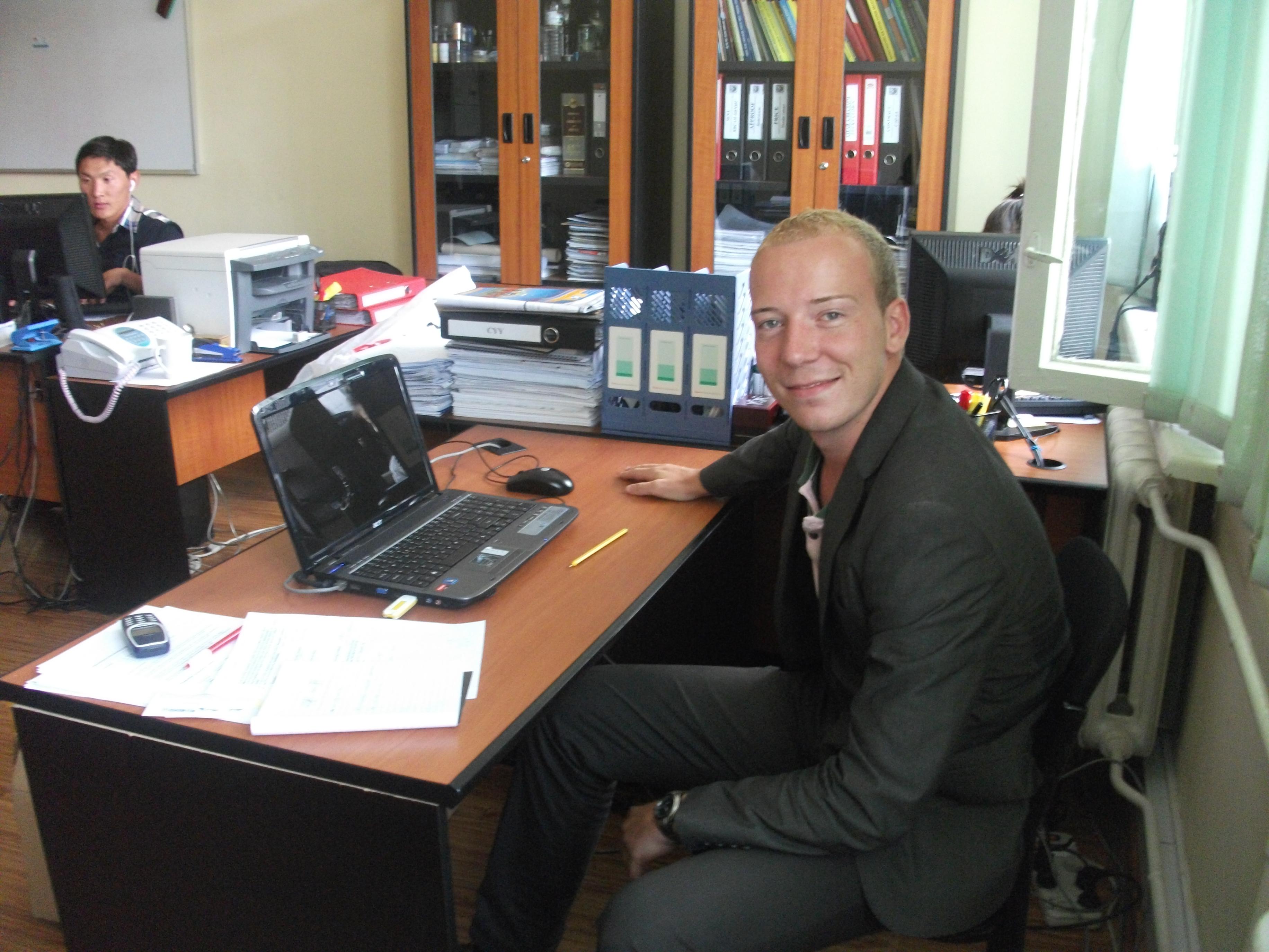 Male Projects Abroad Business Intern sits at a desk at a local firm during his Business Internship in Mongolia. Business Intern poses for a picture at his administration desk during his Business Internship in Mongolia.